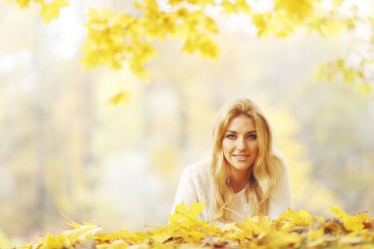 Young woman laying down on the ground covered dry autumnal foliage in beautiful park