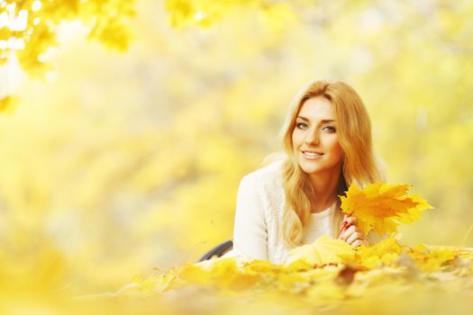 Young woman laying down on the ground covered dry autumnal foliage in beautiful park