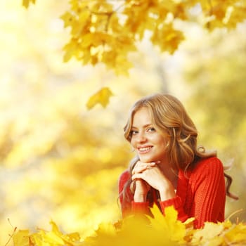 Happy young woman laying on autumn leaves in park