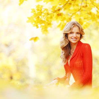 Happy young woman sitting on autumn leaves in park