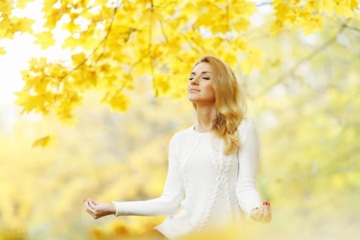 Beautiful young woman meditating outdoors in autumn park