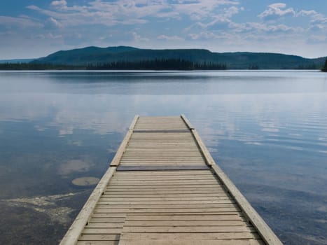 Empty wood plank dock or jetty into dramatic sky reflection on calm still water of Twin Lakes Yukon Territory Canada