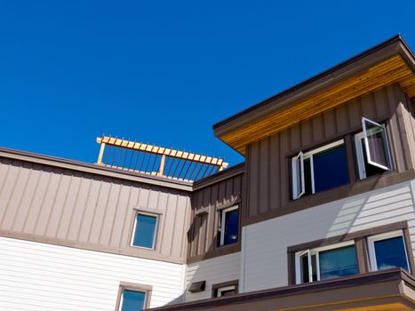 Upper storey detail of timber clad apartment building painted brown and white with open windows under blue sky