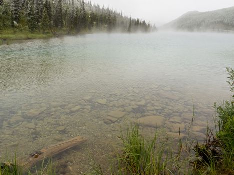 Clear water of boreal forest taiga mountain lake steaming after cold bad weather snow fell in summer