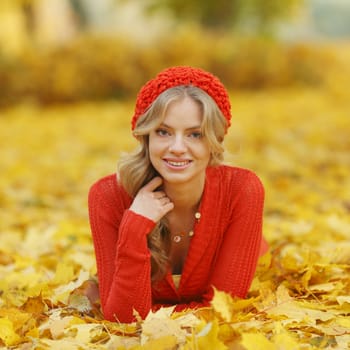 Happy young woman laying on autumn leaves in park