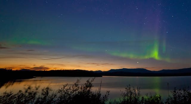Northern lights Aurora borealis at midnight in summer over northern horizon of Lake Laberge Yukon Territory Canada at early dawn