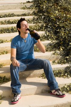 Alcohol addict drinking while sitting on some stairs in a park