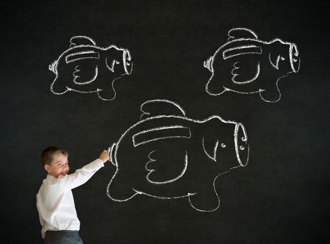 Young business boy drawing flying money piggy banks in chalk on blackboard background