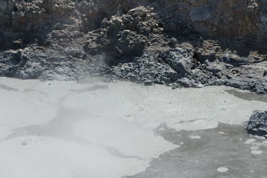Volcanic crater with bubbling water mixed with gray mud 