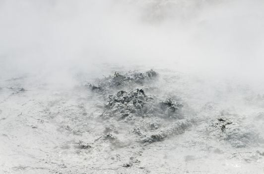 Volcanic crater with bubbling water mixed with gray mud covered by the thick puffy white smoke, Indonesia