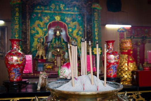 Incense sticks in traditional Chinese temple with a God statue on background.