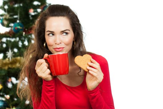 Beautiful woman enjoying a hot drink and gingerbread cookie in front of a Christmas tree. Isolated on white.