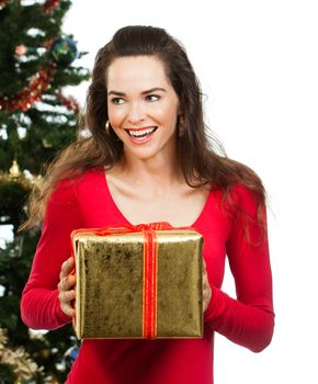 Beautiful happy surprised woman holding a Christmas gift in front of a Christmas tree. Isolated on white.