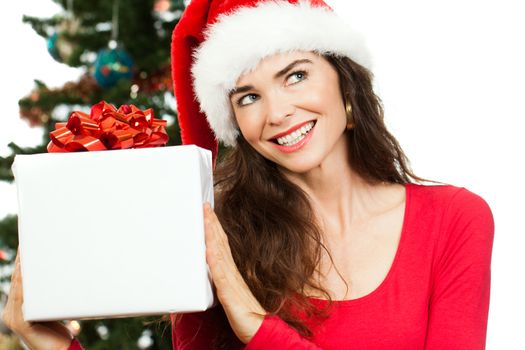 A smiling beautiful woman wearing a Santa hat and holding a big white Christmas present and looking at copy-space. Isolated on white.