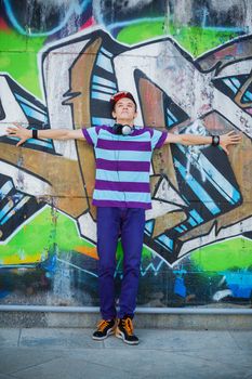 Happy teens boy with headphones near painted wall listening to music