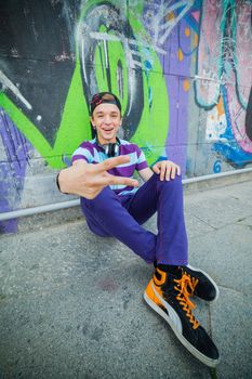 Happy teens boy with headphones near painted wall listening to music