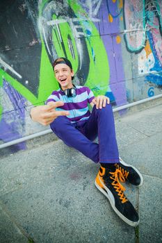 Happy teens boy with headphones near painted wall listening to music