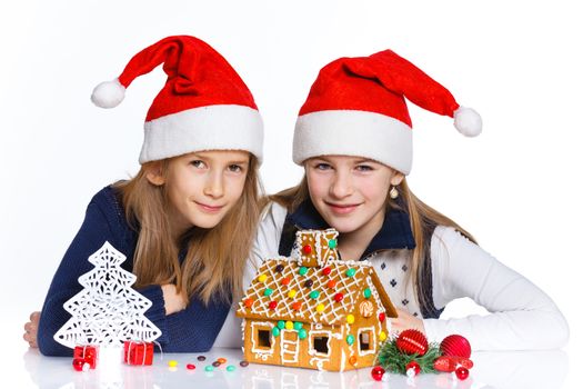 Christmas theme - Two smiling girl in Santa's hat with gingerbread house, isolated on white