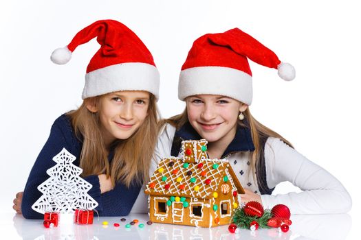 Christmas theme - Two smiling girl in Santa's hat with gingerbread house, isolated on white