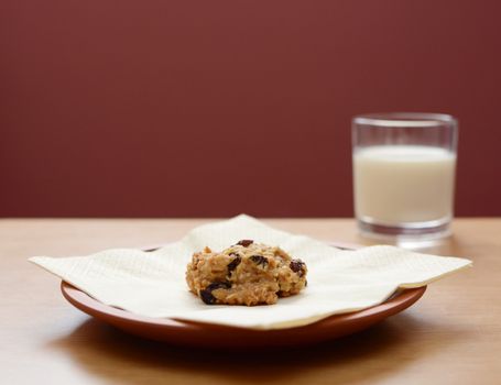 Oatmeal raisin cookie on a plate with a glass of milk in the background