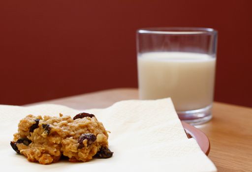 Closeup of a freshly baked oatmeal raisin cookie with a glass of milk
