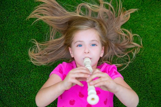 Blond kid children girl playing flute lying on grass backyard lawn