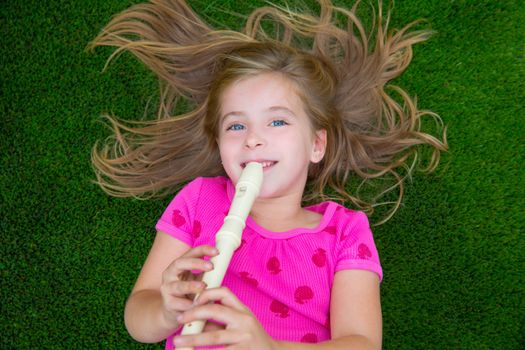 Blond kid children girl playing flute lying on grass backyard lawn