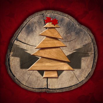Wooden Christmas tree and red comet on on section of tree trunk and red velvet background
