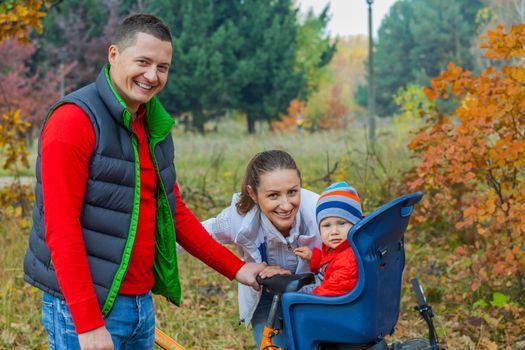 Family with baby on bikes in the autumn park.