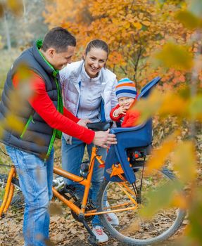 Family with baby on bikes in the autumn park.