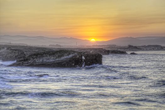 Beautiful sunset and stone arches on Playa de las Catedrales during inflow, Spain