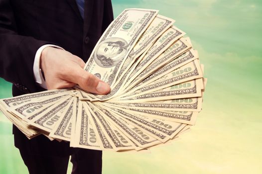 Business Man Displaying a Spread of Cash over Vintage Sky Background