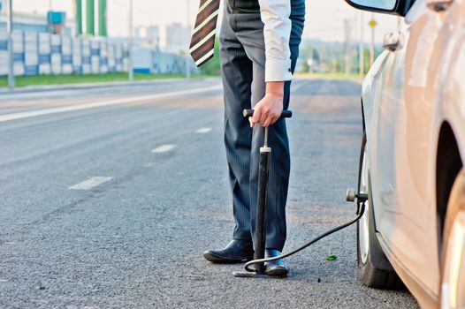 man in a business suit pumps hand pump wheel of a car