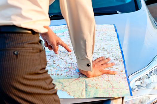 Businessman looking at a map spread out on the hood of a car