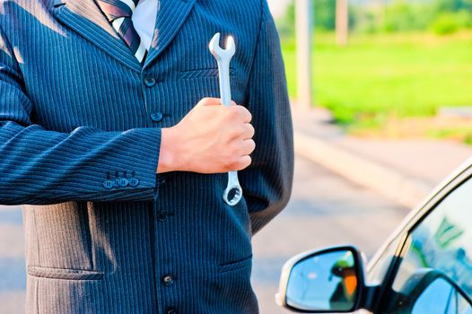 a man in a business suit with a car holding a wrench