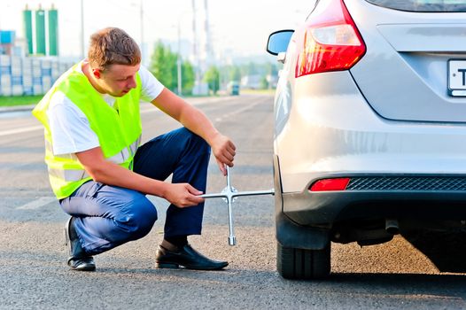 mechanic in a vest tie the wheel to the car on the road