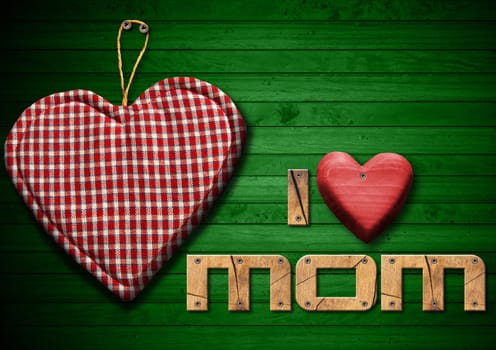 I Love Mom written with wooden letters and red wooden hearts, handmade cloth heart hanging on green wooden background