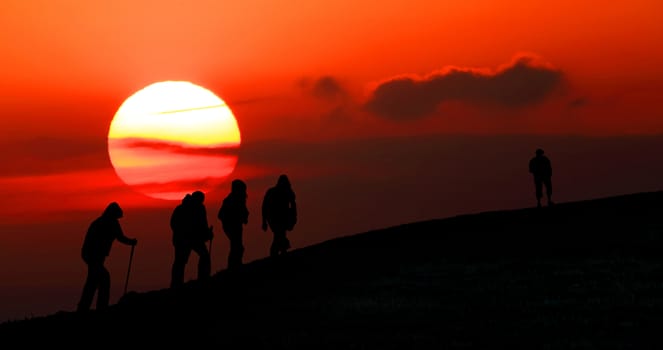 Group of tourists take to the mountains at sunset. Silhouette
