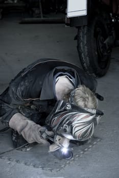 a mechanic welding the exhaust of a motorbike in a garage