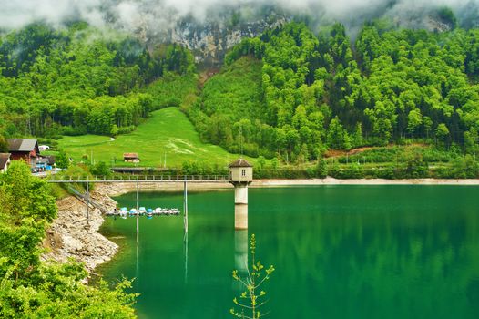 Beautiful emerald mountain lake in Switzerland under low clouds