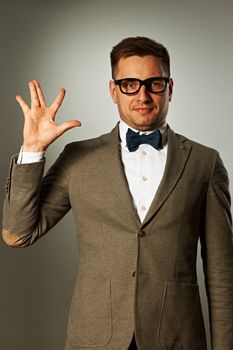 Nerd in eyeglasses and bow tie says Hello against grey background