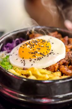 bibimbap in a heated stone bowl ,  korean style food ( rice , meat , fried egg and mix vegetable )
