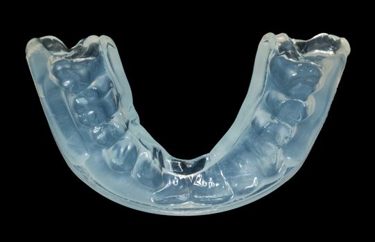 Macro close up of a plastic teethguard to stop wear due to teeth grinding at night isolated against black background. Often caused by tension and worry.