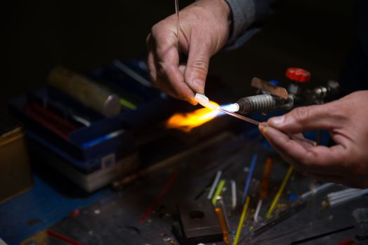 master glassblower shapes the glass warmed by the burner flame