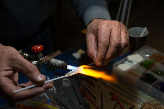 master glassblower shapes the glass warmed by the burner flame