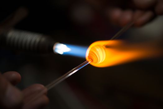 master glassblower shapes the glass warmed by the burner flame