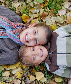 Happy kids lying on autumnal ground covered with dry leaves