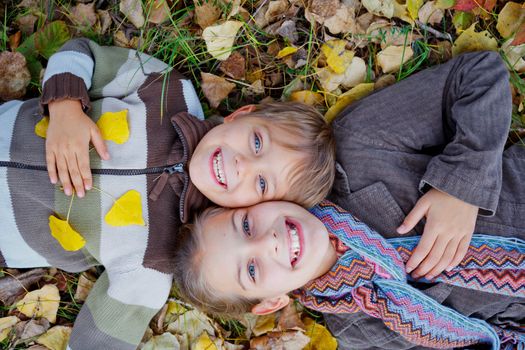 Happy kids lying on autumnal ground covered with dry leaves