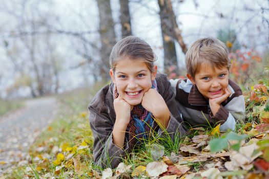 Happy kids lying on autumnal ground covered with dry leaves