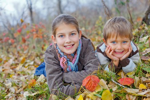 Happy kids lying on autumnal ground covered with dry leaves